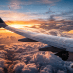 Asas de um avião comercial cortando o ar acima das nuvens durante o pôr do sol.